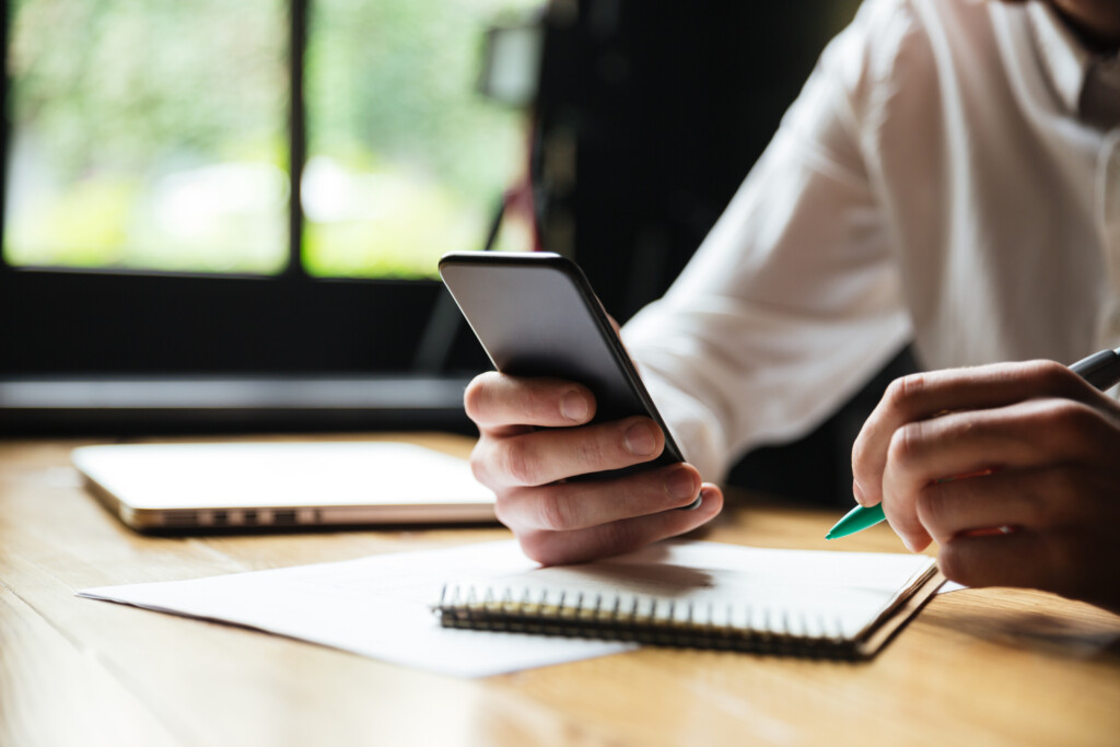 cropped-photo-young-man-white-shirt-holding-smartphone-while-resting-after-paperwork