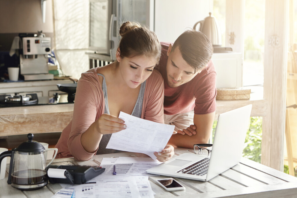 young-couple-managing-finances-reviewing-their-bank-accounts-using-laptop-computer-calculator-modern-kitchen-woman-man-doing-paperwork-together